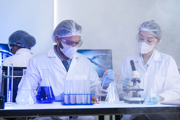 A diverse team of scientists collaborates in a high-tech biotech lab. A senior researcher mentors...
