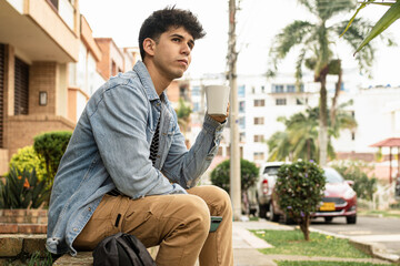Early day routine with coffee and cellphone outside. Colombian man in an urban garden, surrounded...