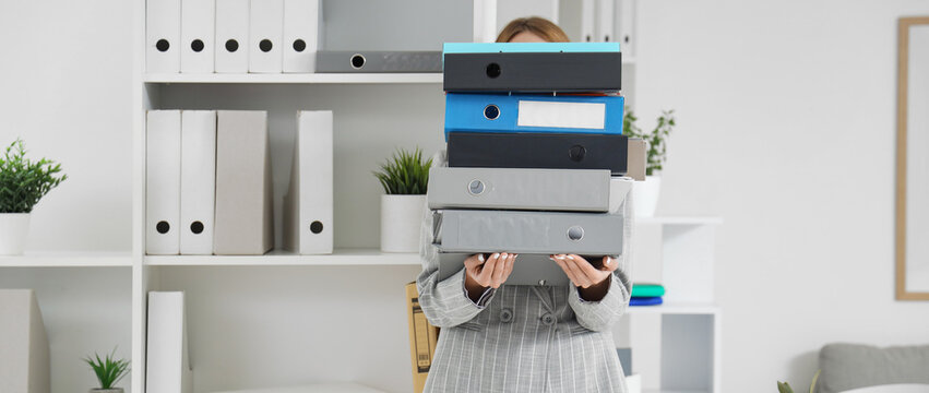 Young businesswoman with stack of document folders in office