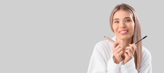 Pretty young woman holding mascara on grey background with space for text