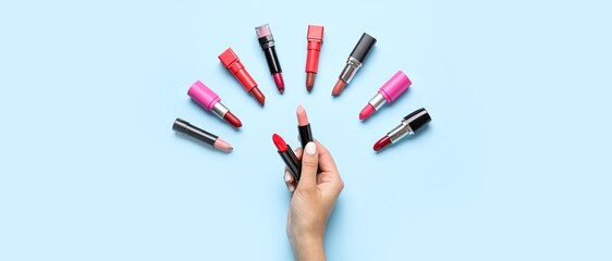 Female hand and many different lipsticks on light blue background, top view