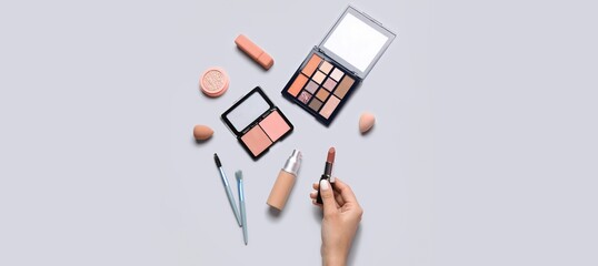 Female hand and different decorative cosmetics on grey background, top view