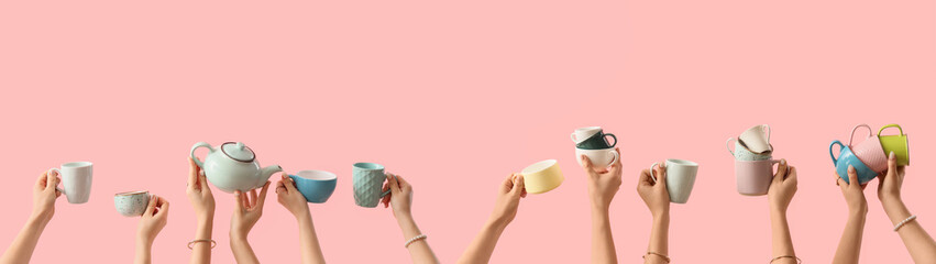 Female hands with teapot and mugs on pink background