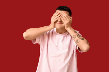 Handsome ashamed young man covering face with hands on red background