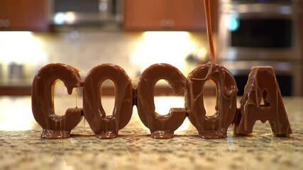 The word "COCOA" in brown, blocky letters with caramel drizzles on a speckled marble surface, blurred kitchen background - Powered by Adobe