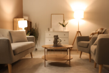 Blurred view of modern living room with grey sofa, armchairs and glowing lamps at evening