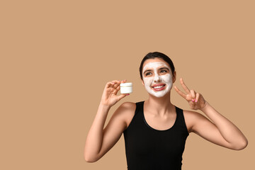 Young woman with facial mask showing victory gesture on color background