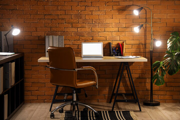 Interior of dark office with workplace, blank laptop and glowing lamps at night