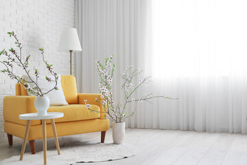 Vases with blooming branches and yellow armchair in interior of light living room