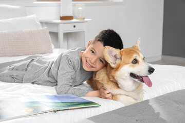 Little happy Asian boy reading book with cute Corgi dog lying at home