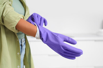 Woman putting on rubber gloves in kitchen, closeup