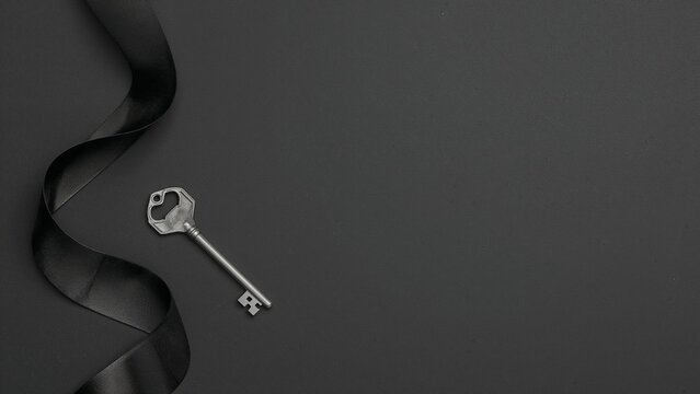 Lying silver skeleton key on dark tabletop, with coiled black satin ribbon, copy space - Powered by Adobe