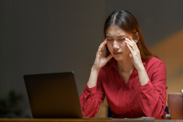 Young Asian businesswoman feeling tired and stressed from overworking late at night in office using...