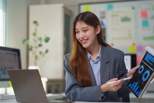 Young professional woman using laptop and showing charts and graphs, discussing financial results with colleagues during video call