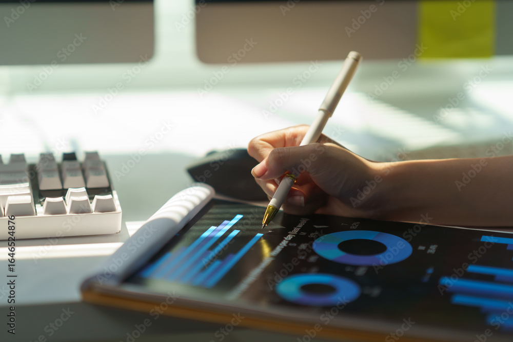 Poster businesswoman using pen and analyzing financial charts and graphs displayed on digital tablet while 