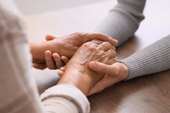 Young woman with grandmother holding hands on table, closeup. Care concept