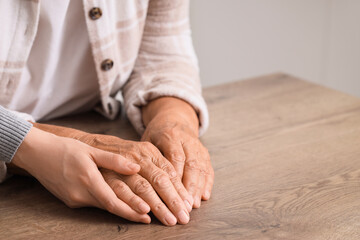 Young woman with grandmother holding hands on table, closeup. Care concept