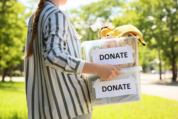 Young woman holding containers with clothes for donation outdoors
