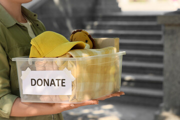 Young woman holding container with clothes and toy for donation outdoors