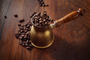 Coffee beans in the turkish dzezva coffee pot on wooden background. Top view.