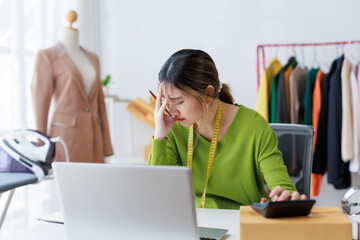 Young woman calculating expenses and feeling overwhelmed by stress while managing her tailor shop...
