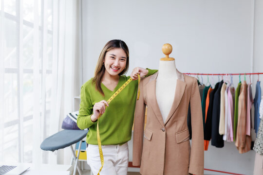Smiling Asian fashion designer measuring a suit jacket on a mannequin in her stylish atelier, showcasing her creativity and skill - Powered by Adobe
