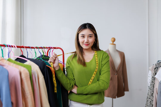 Asian fashion designer holding measuring tape and working in her workshop, startup small business SME, dressmaker on the job - Powered by Adobe