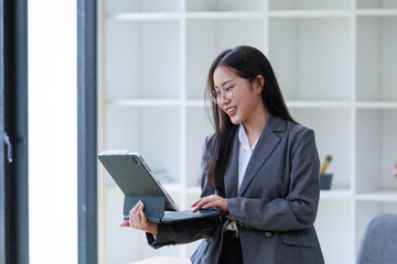 Smiling businesswoman using a digital tablet and keyboard while working in a bright, modern office filled with natural light
