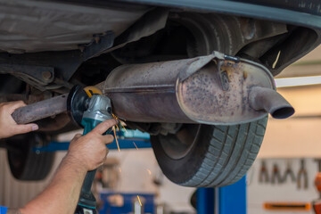 Repairer cuts old silencer on car by angle grinder. Master replacing of  muffler of exhaust system...
