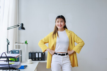 Young asian businesswoman smiling with hands on hips in her modern office, showing confidence and...