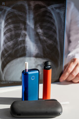 Doctor holds x-ray of lungs with e-cigarettes and vape in background. 