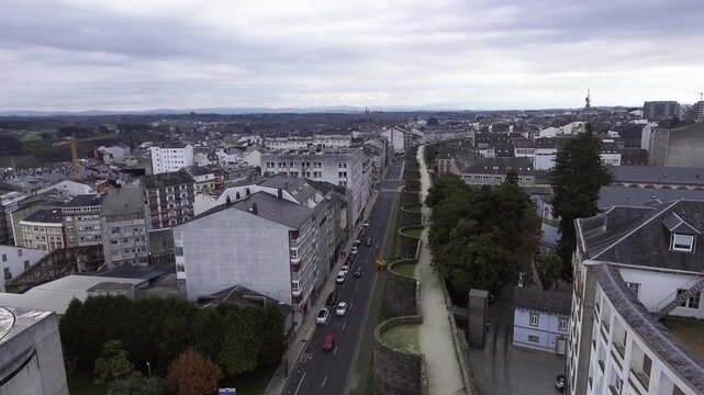 Drone takeoff with tilt down over Lugo&rsquo;s Roman Wall at Porta Falsa. Vehicles on the road and people walking along the adarve. UNESCO World Heritage site in Galicia, Spain.