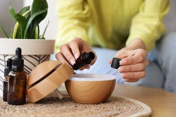 Woman pouring essential oil into air humidifier on table at home, closeup
