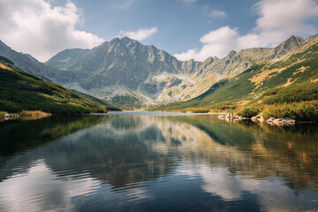Naklejka premium breathtaking summer landscape of lake against majestic mountains reflecting soft clouds above