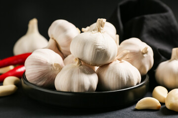 Plate with fresh garlics on black background