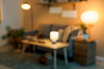 Blurred view of dark living room with glowing lamps, sofa and table at night