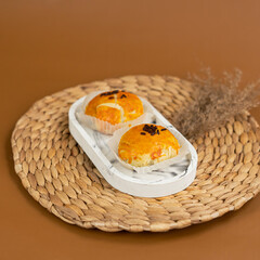 Two golden brown bakpia with glossy egg wash and chocolate sprinkles on top, served on a white...