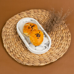 Two golden brown bakpia with glossy egg wash and chocolate sprinkles on top, served on a white...