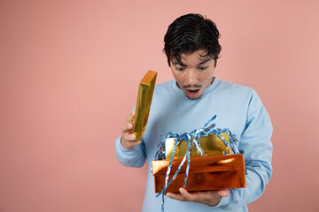 Surprised man opening a gift box with blue confetti on a pink background, surprise gift concept