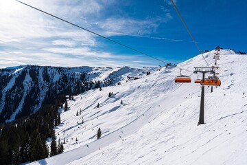 A beautiful winter scene at a ski resort, with a chairlift going up a snow-covered mountain under a...