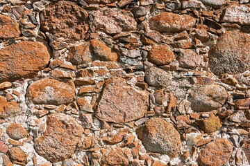 A weathered stone wall with a rugged texture showcases an array of colorful brown and gray rocks. This aged exterior serves as an ideal backdrop for textures, overlays, and artistic designs.