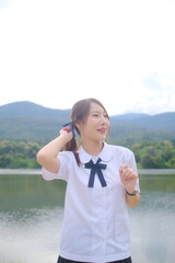 A girl wearing a white shirt and a blue bow tie is standing by a lake. A Student girl concept