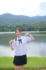 A girl in a school uniform poses for a picture by a lake. A Student girl concept