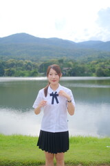 A woman in a school uniform stands in front of a lake. A Student girl concept