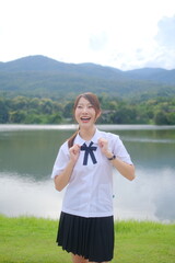 A woman in a school uniform is smiling and posing for a picture by a lake. A Student girl concept