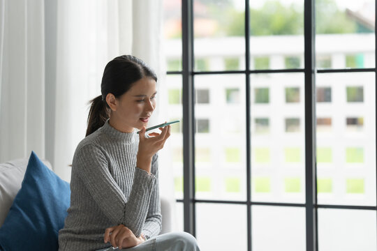 Asian woman using voice assistant on smartphone at home conversation with online assistant Voice chat bot conversational AI Modern Technologies.