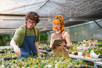 Obraz premium Young Asian Man and Woman Plant Research Working Together in Greenhouse Inspecting Blooming Cactus Flowers with Tablet Eco-Friendly Research and Data