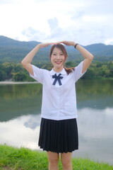 A woman in a school uniform stands in front of a lake, smiling. A Student girl concept