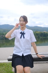 A woman in a school uniform sits on a bench by a lake. A Student girl concept