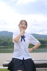 A girl in a school uniform is sitting on a bench by a lake. A Student girl concept